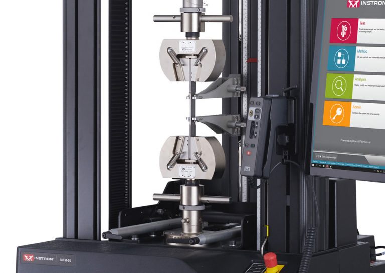 Close-up of manual wedge grips and an automatic contacting extensometer mounted on an Instron 68TM-50 table model universal testing system, with the Bluehill Universal software operator dashboard in view.