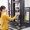 Test machine operator inserts plastic specimen into Instron pneumatic side action tensile grips mounted on 68TM universal testing system with Bluehill Universal software and Advanced Video Extensometer.