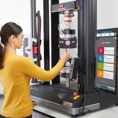Test machine operator inserts plastic specimen into Instron pneumatic side action tensile grips mounted on 68TM universal testing system with Bluehill Universal software and Advanced Video Extensometer.